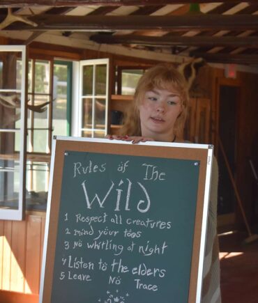 camper standing next to sign with camp values and rules of the outdoors