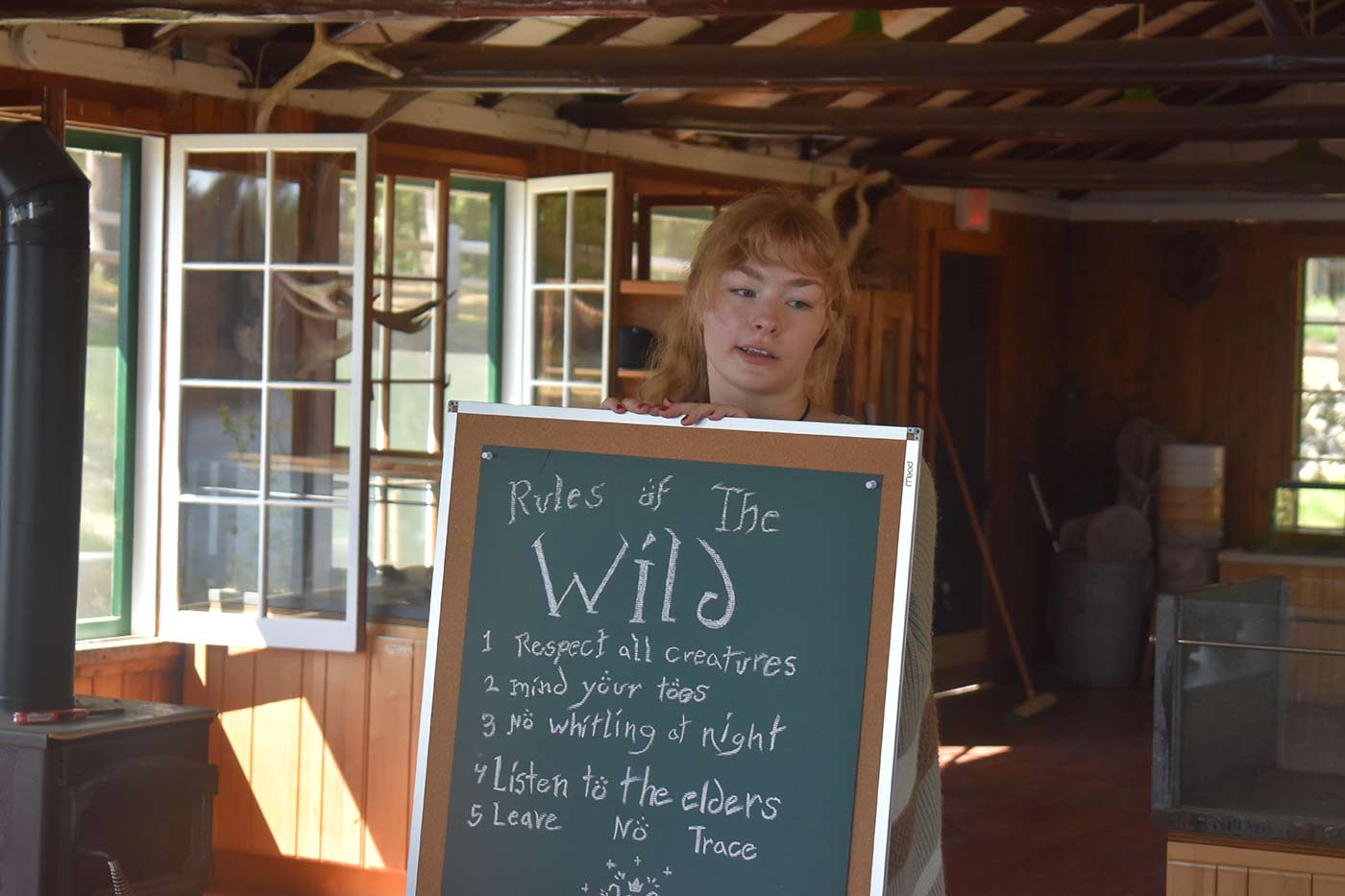 camper standing next to sign with camp values and rules of the outdoors